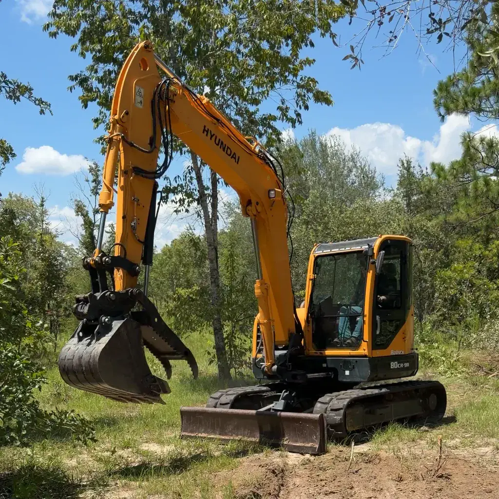 Yellow Hyundai Robex 80CR-9A excavator on a wooded Florida property